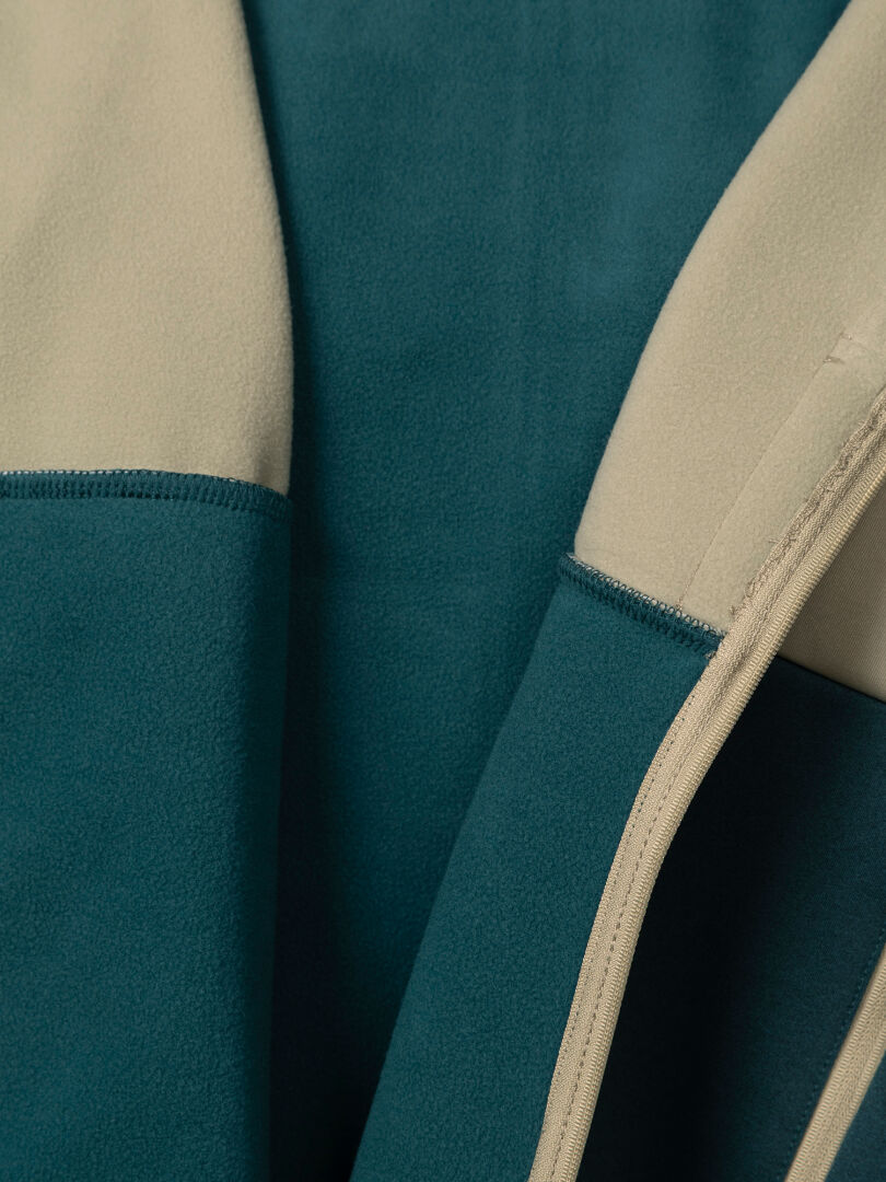 Close-up of a Halti Seiland Layer Jacket Women’s in a teal and beige color-blocked stretch fleece with a central zipper.