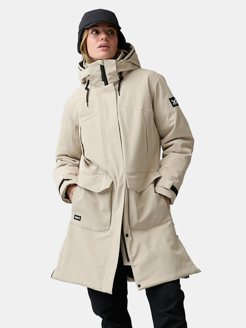 Woman in Halti Kallio DX Parka, black pants, and cap, stands with hands in parka pockets.