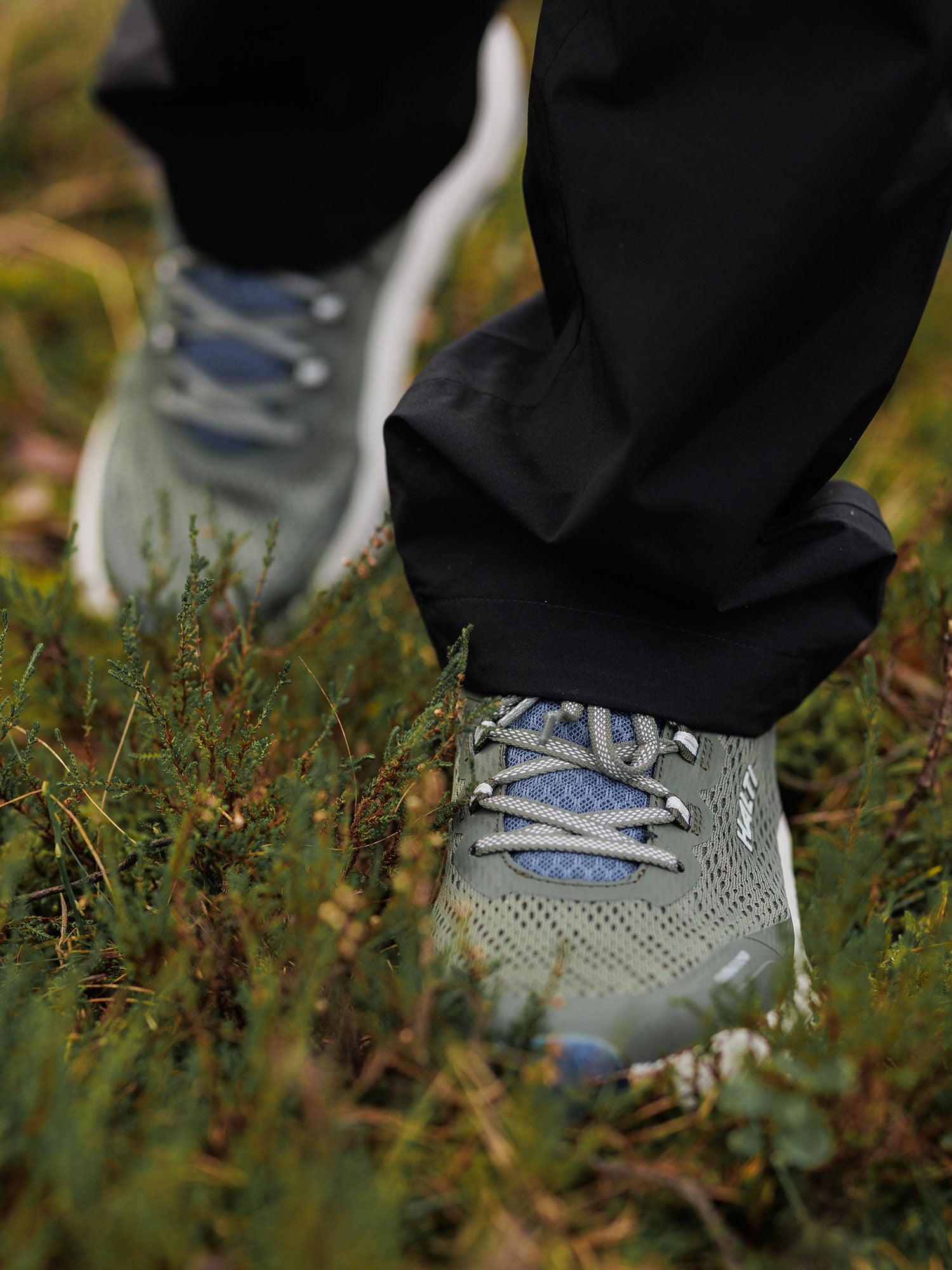 Person wearing Halti Rapid 2 Sneaker Men's and black pants standing on grass and small plants outdoors.