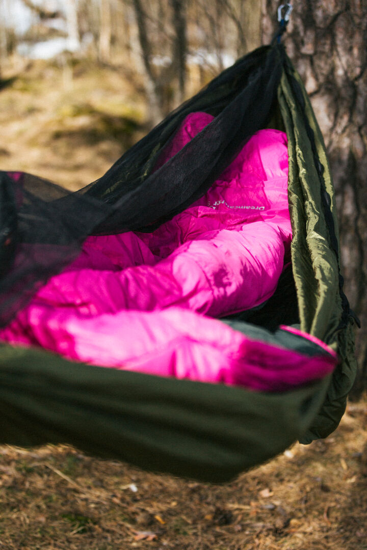 Person in a Halti Dreamcatcher 30 M sleeping bag with thermal collar rests outdoors in a hammock under a black net.