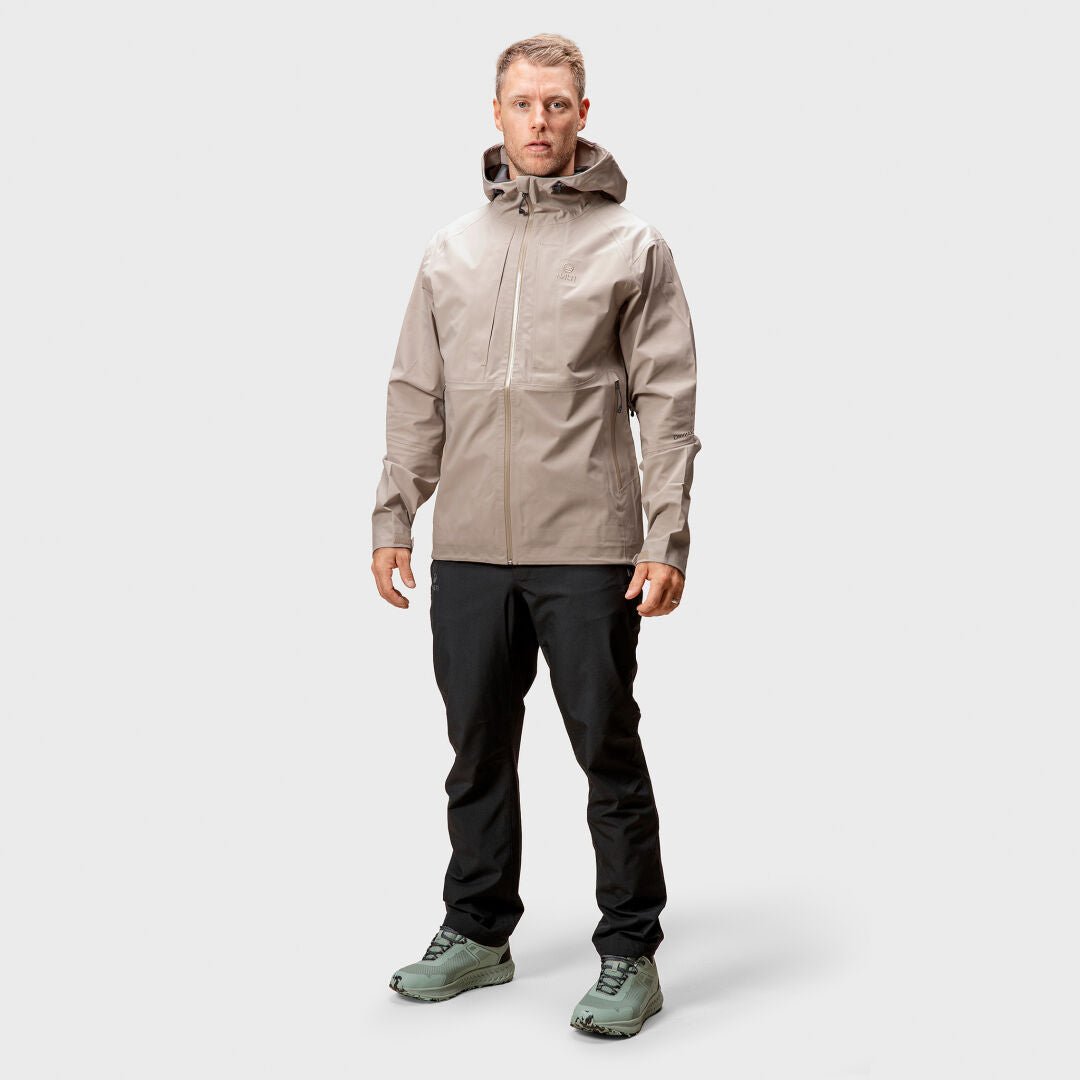 A man faces forward in a Halti Kaarna Mens DX 3L Shell Jacket, black pants, and green sneakers.