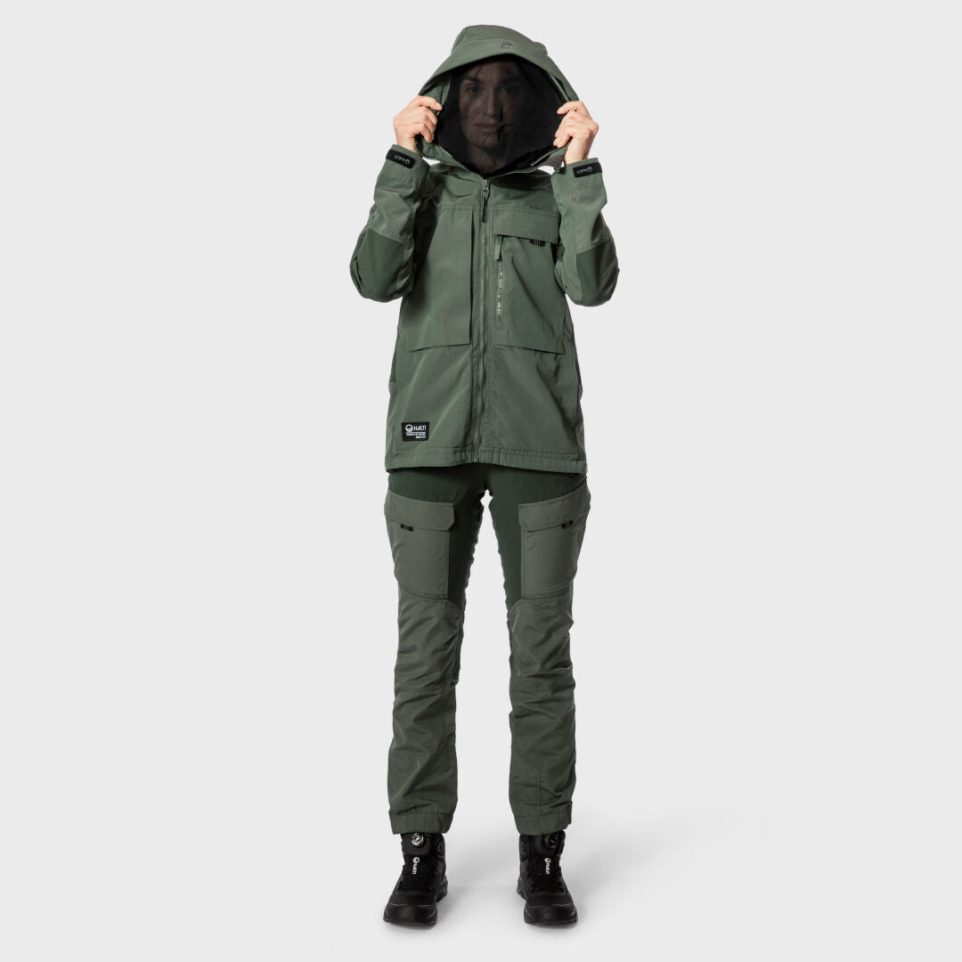 A person wears Halti Hiker Womens Ventilated Pants and a green hooded jacket, standing against a plain light background.