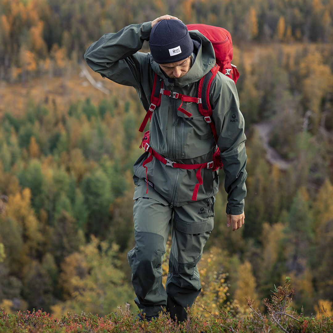 Wearing a green-red Halti Hiker 3L DX Ventilated Jacket, the hiker explores the autumn forest, gazing down thoughtfully.