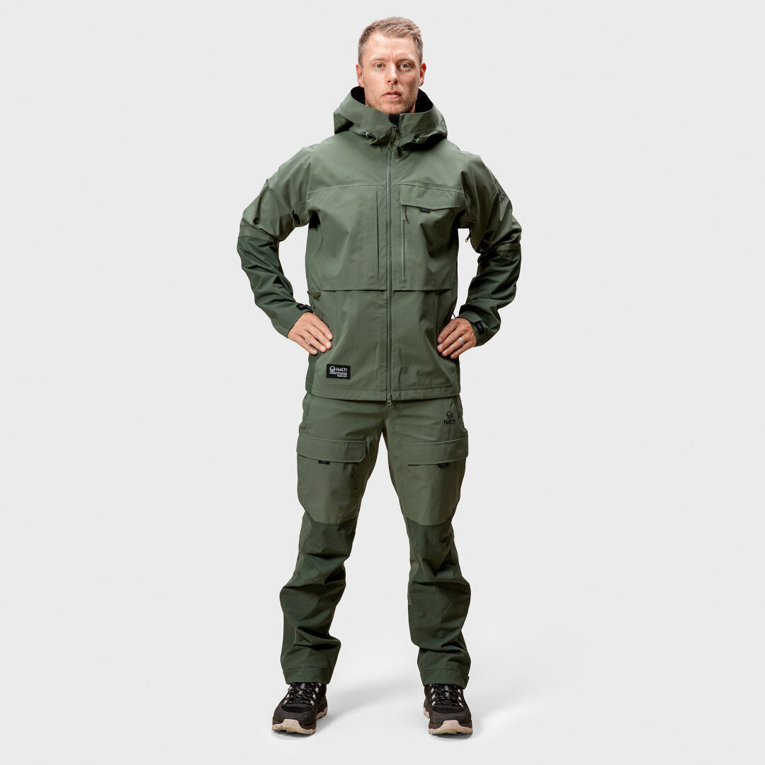 Person wears a green Halti Hiker 3L DX Ventilated Jacket and pants, hands on hips, standing against a plain background.