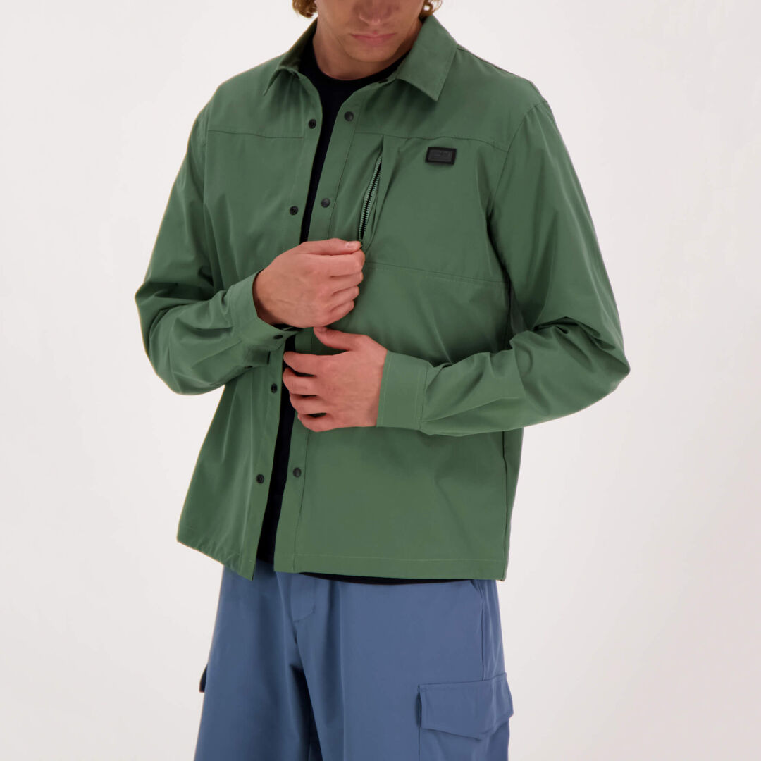 Model wearing the Halti Bluusi Unisex Shirt in green, opening the chest pocket against a plain background.