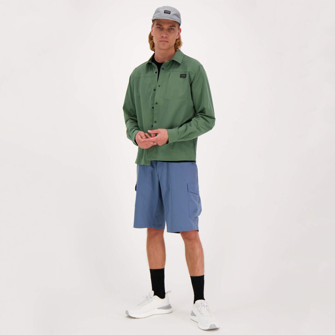 A person stands against a plain background in Haltis Bluusi Unisex Shirt, blue shorts, and white sneakers.