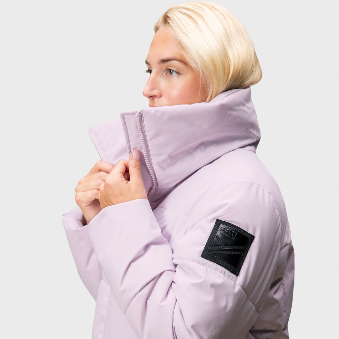 A woman wearing a Halti Penger Winter Jacket with a high collar and black sleeve patch, facing to the side.
