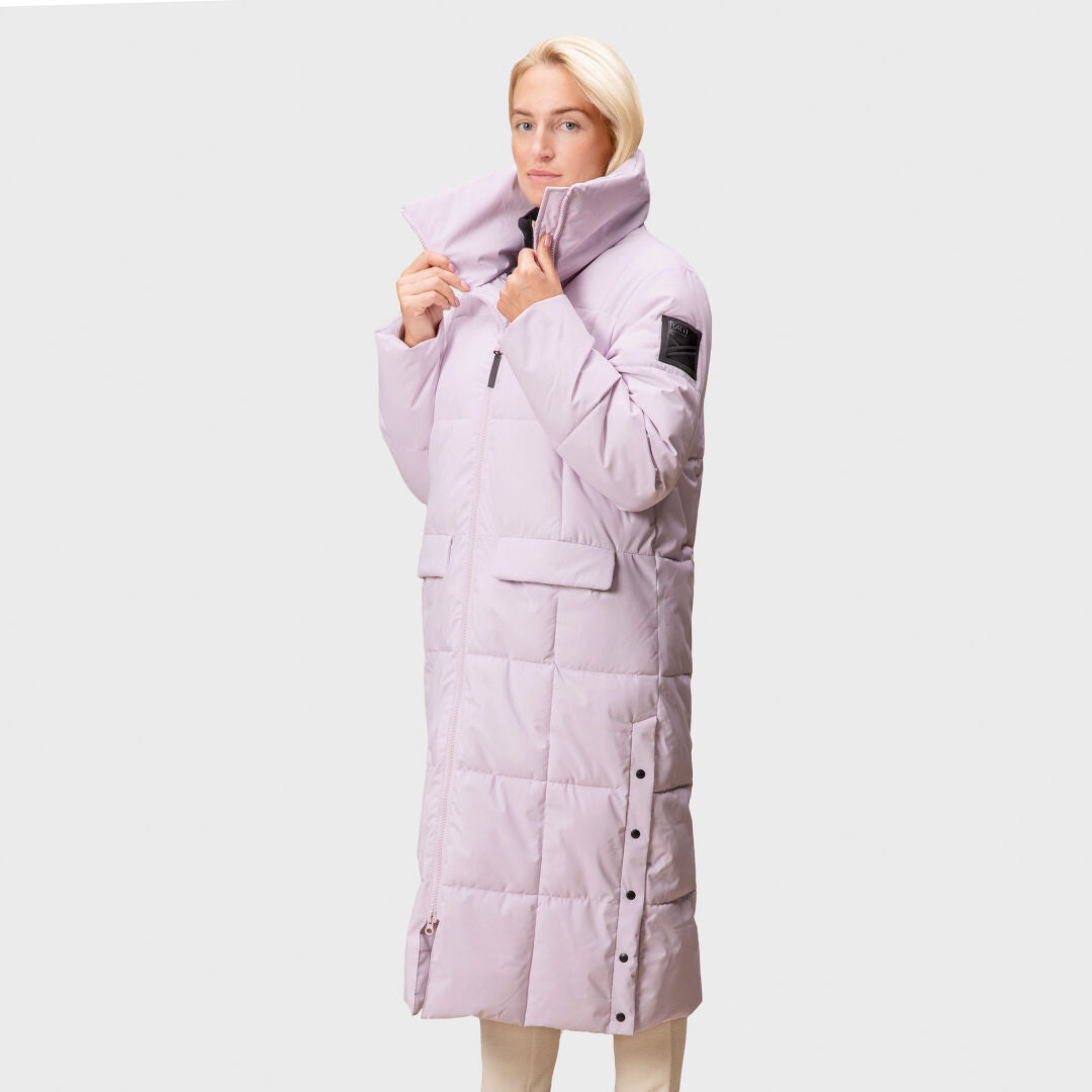 A woman wears a long, light purple Halti Penger Winter Jacket against a plain light gray background.