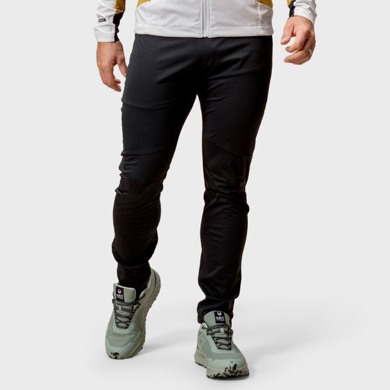 A person wears Halti Veloce XCT Pants, a white jacket, and gray trail running shoes against a plain background.