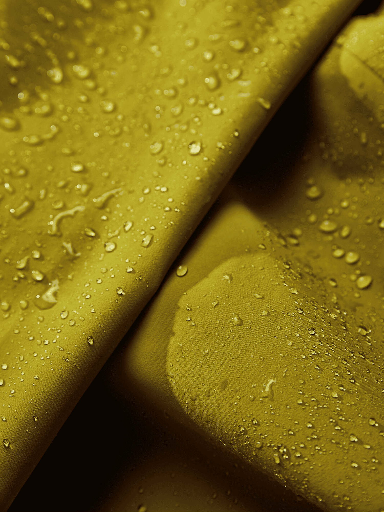Close-up of a mustard yellow fabric with water droplets on its surface, showing the materials water-repellent properties and subtle texture with visible folds and creases.