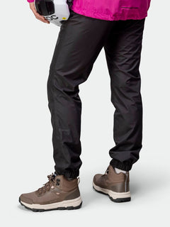 Person in black pants, pink jacket, and Halti Fara 3 DX Mid Outdoor Shoe holds a white helmet, facing away.