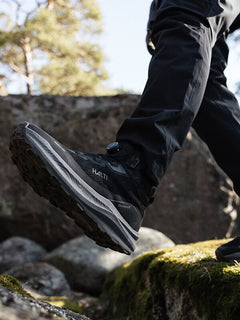 Wearing black Halti Rapid Mid Freelock DX Shoes and black pants, a person steps onto a mossy rock outdoors.