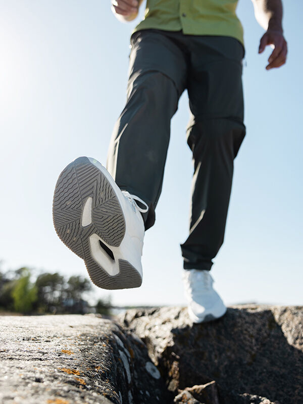 A man wearing Halti Syke Sneaker steps over a rock gap, low angle shot with a clear sky in the background.