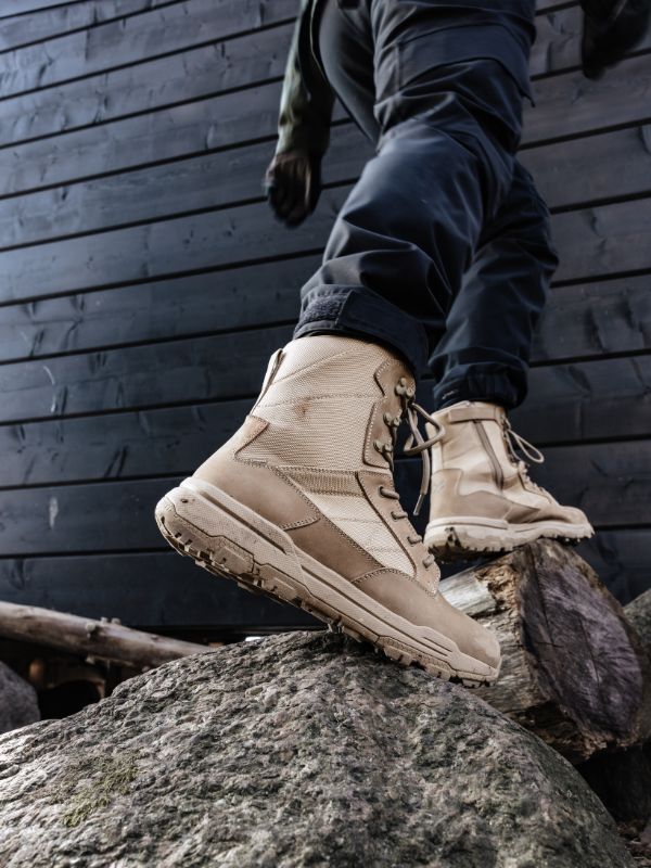 A person in Halti Regis DX Boot Men's and dark pants steps on large rocks near a dark wooden wall.