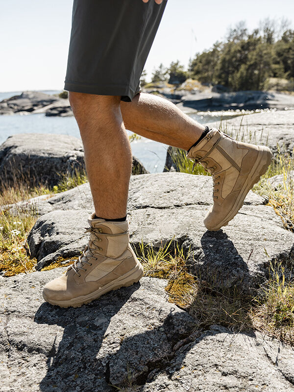 Wearing Halti Regis DX Boot Men's and shorts, person hikes on rocky terrain near water with trees in the background.
