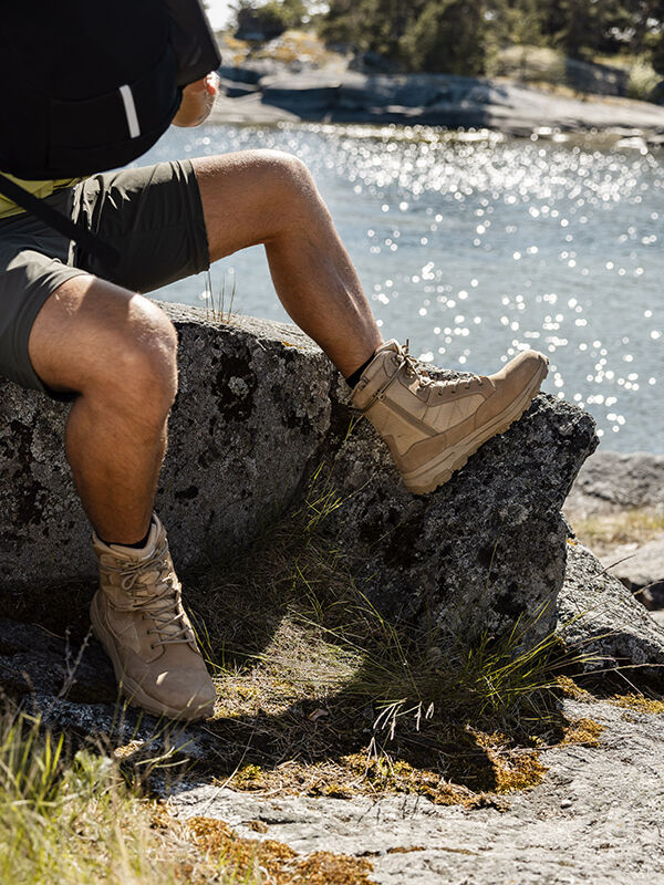 Wearing Halti's Regis DX Boot Men's, a person in shorts sits on a rock by sunlit water.