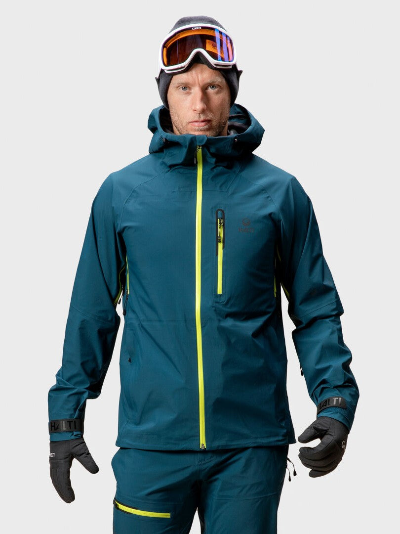 A person wears the Halti Alpine Unisex 3L DrymaxX Shell Jacket, matching pants, gloves, and ski goggles facing the camera.