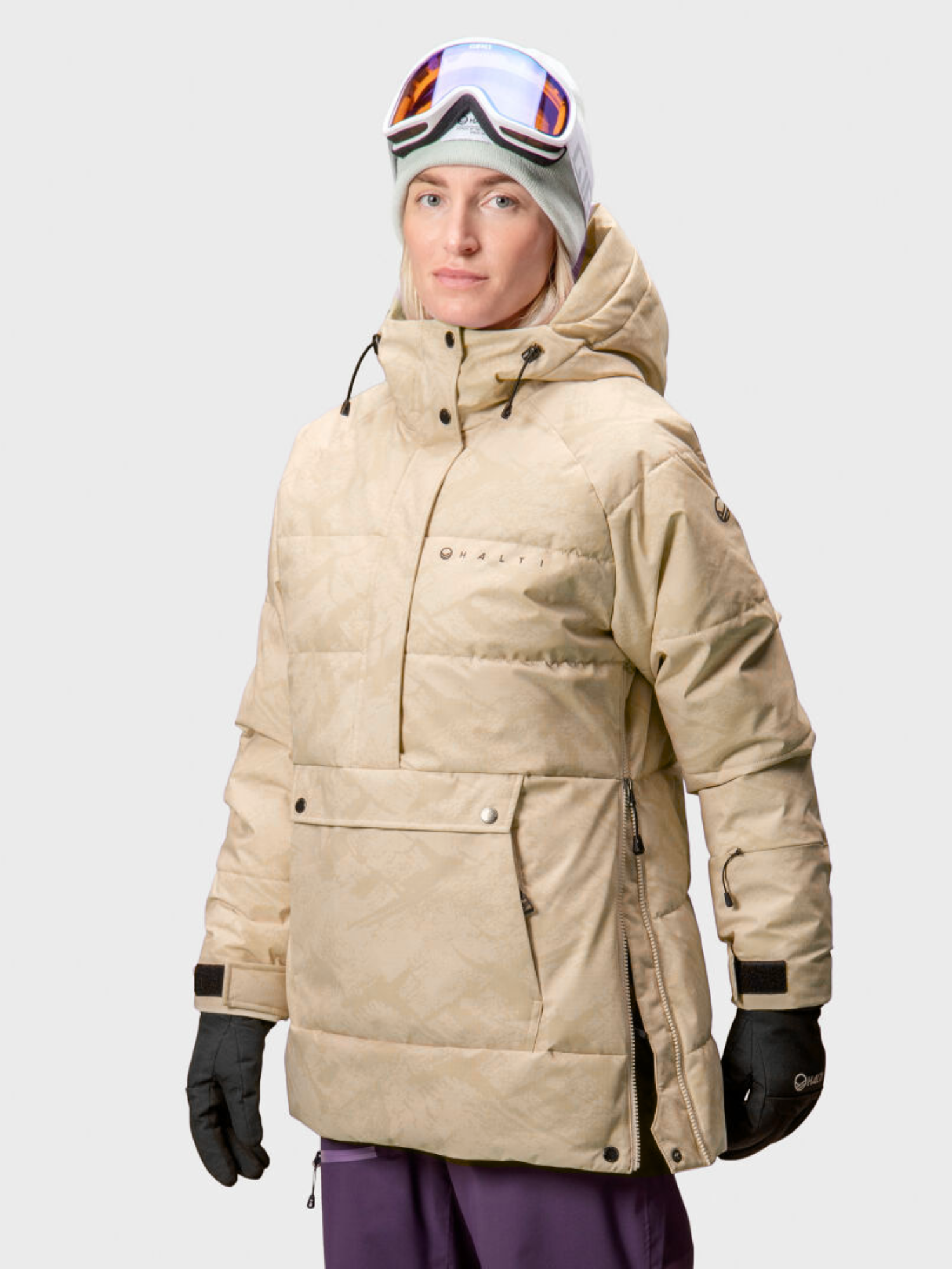 A person faces forward in a Halti Chowper Ski Anorak Women's, black gloves, gray beanie, and ski goggles.