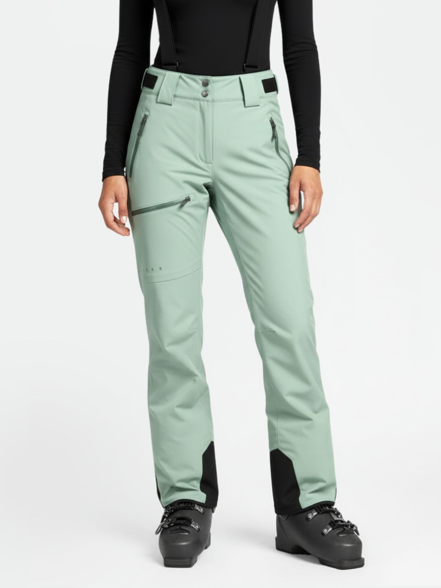 A person wears Halti Carvey DX Ski Pants Women's in light green, a black long-sleeve top, and black ski boots.