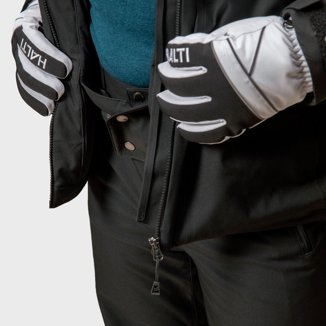 A person wears a black Halti Vertica DX Ski Jacket Men’s and pants, with gloved hands resting on the open jacket.