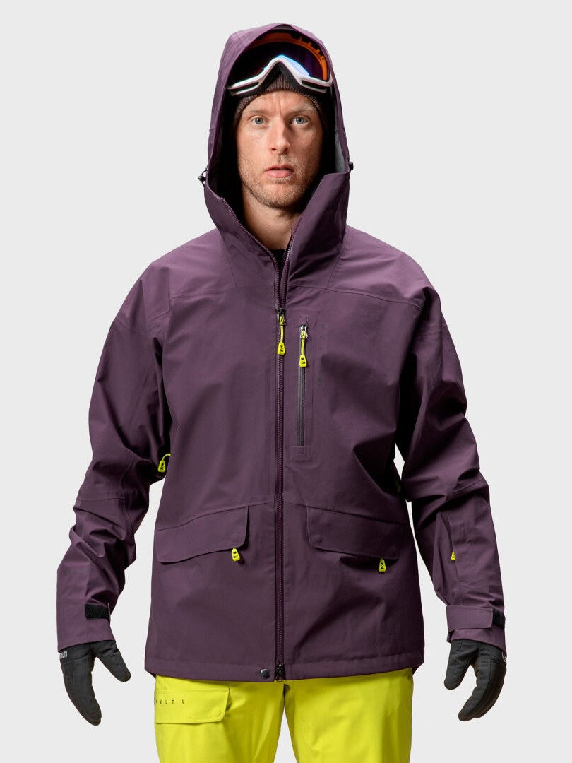 A man in a Halti Settler 3L DrymaxX Ski Jacket, yellow pants, and ski goggles stands facing forward.