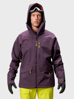 A man in a Halti Settler 3L DrymaxX Ski Jacket, yellow pants, and ski goggles stands facing forward.