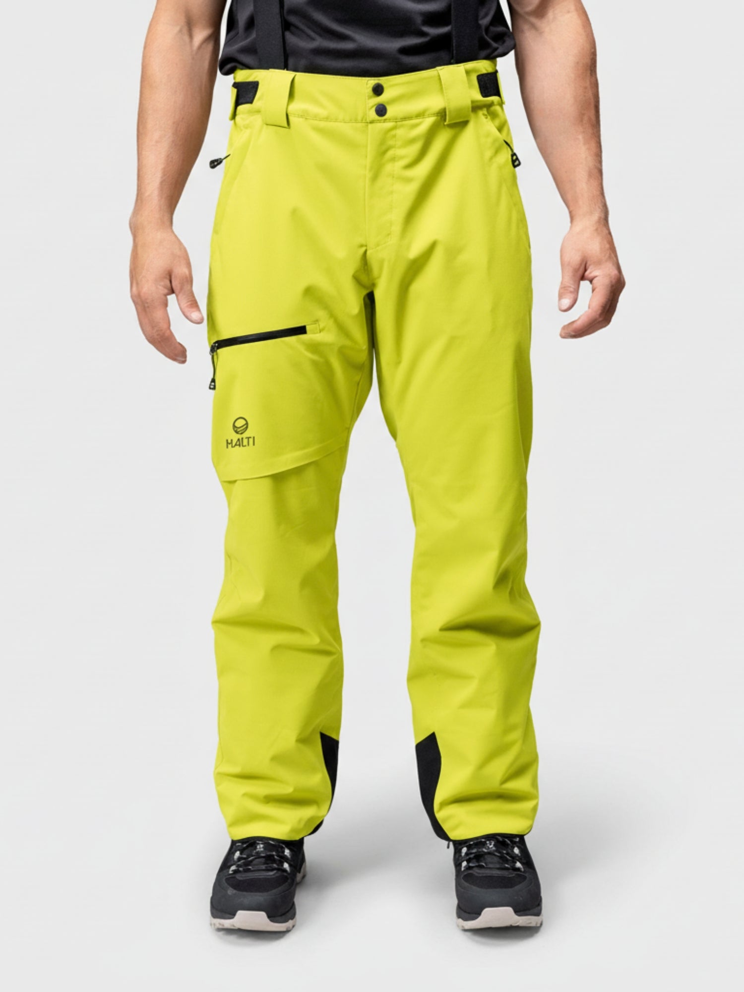 A person wears Halti Carvey DrymaxX Men's Ski Pants in bright yellow with black accents and black shoes against a plain background.