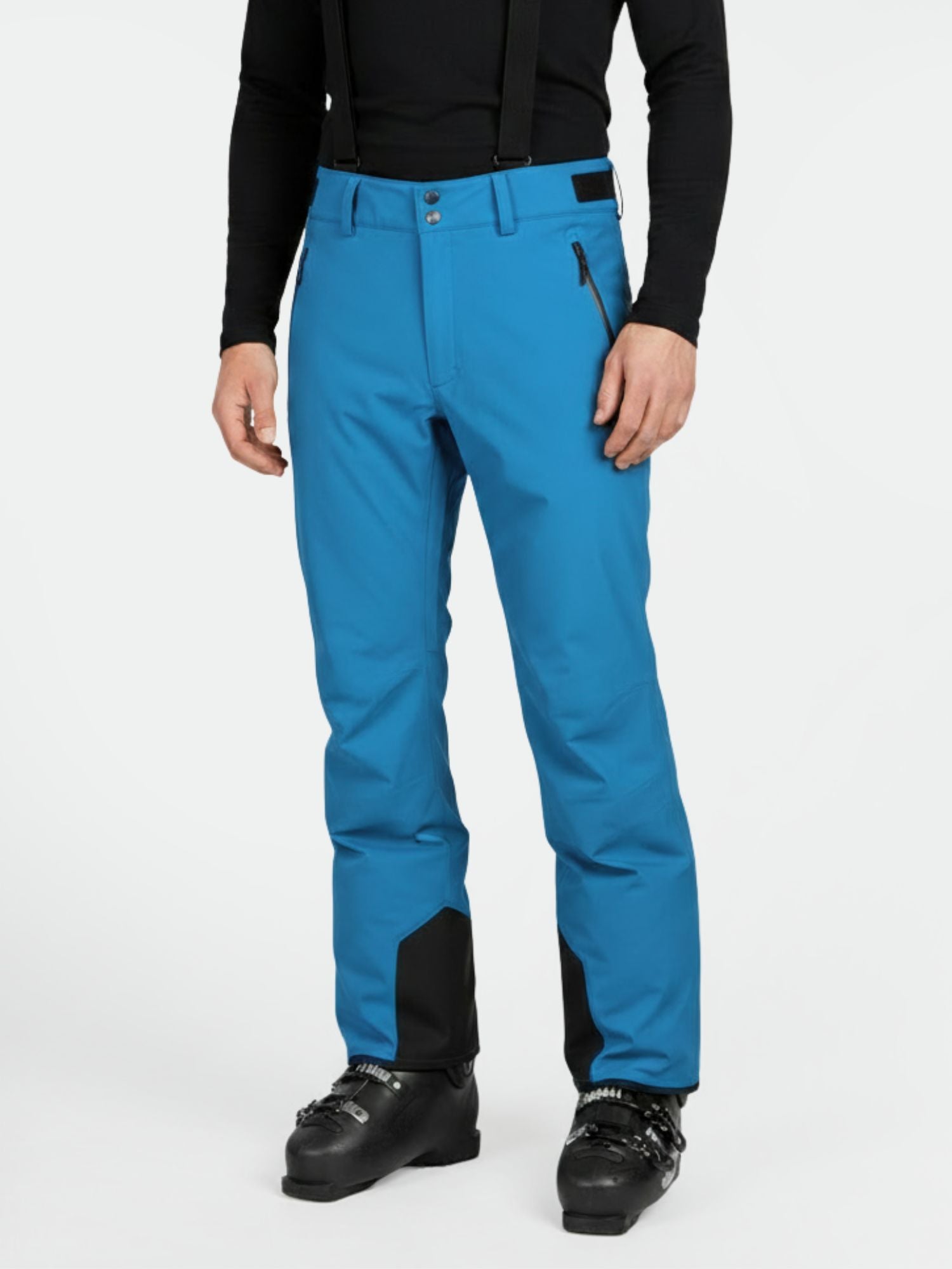 A person in Halti Trusty DrymaxX Ski Pants (bright blue) with black suspenders, ski boots, and a black long-sleeve top.