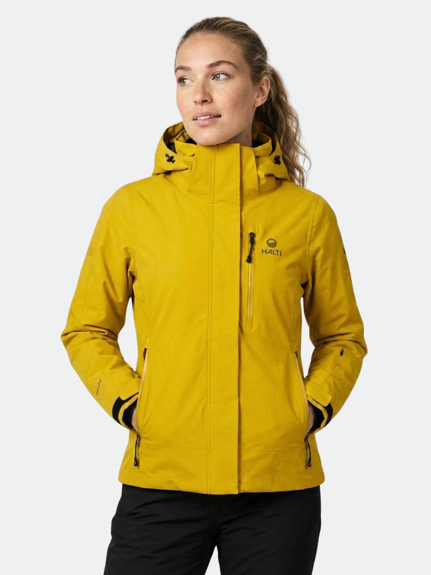 Woman wearing a Halti Radius DX Ski Jacket in yellow with hands in pockets, looking to the side against a plain background.