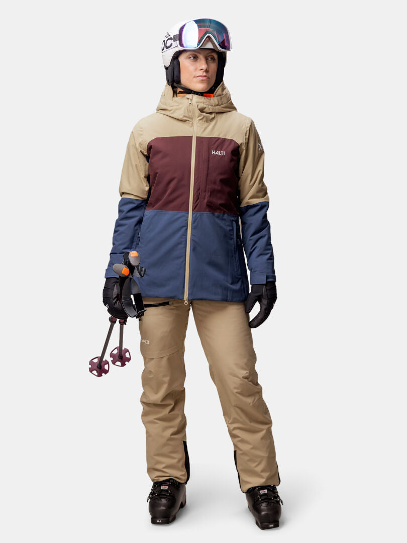 Person in ski gear wearing Halti Gracer DX Ski Jacket Women's, beige pants, helmet, goggles, gloves, and ski boots.