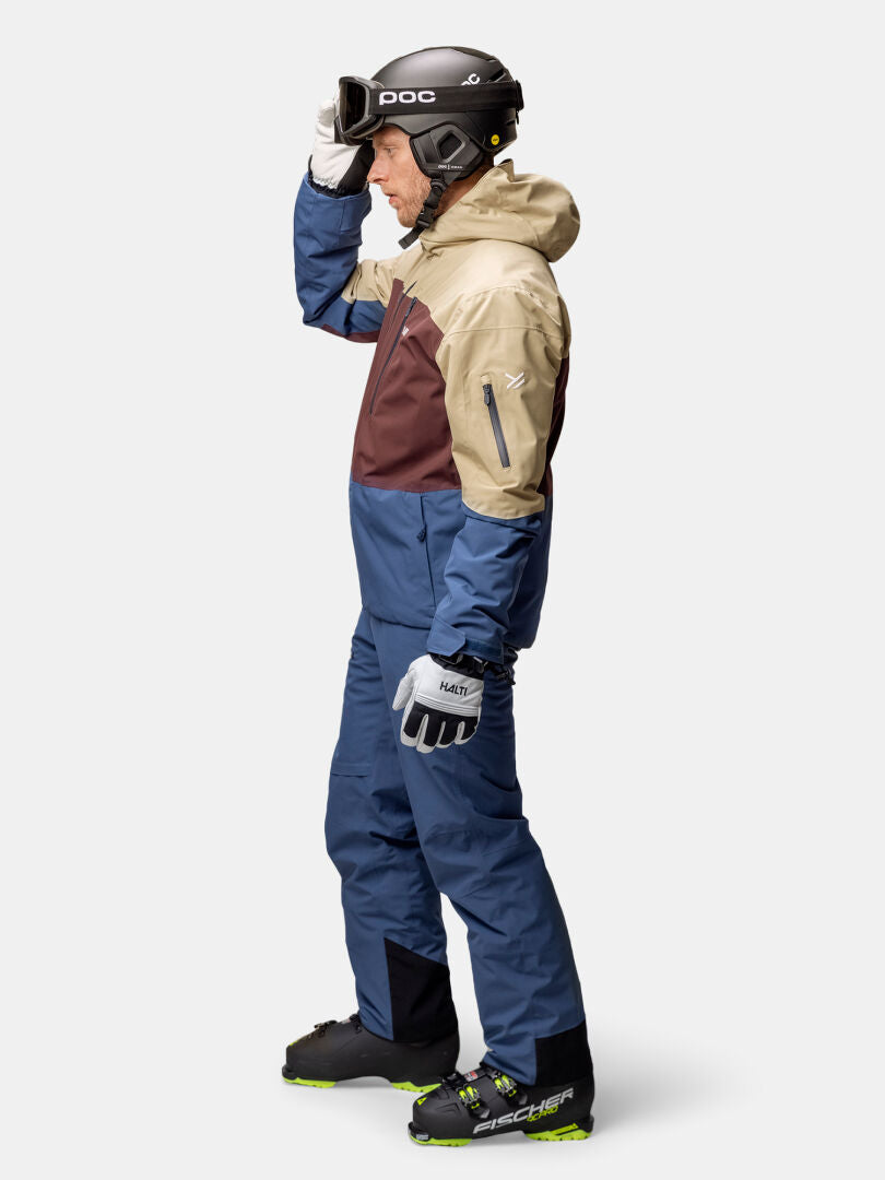 Wearing the Halti Melvik Dx Ski Jacket Men's, he holds goggles against a plain white background.