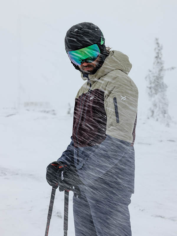 A skier wears the Halti Melvik Dx Ski Jacket Men's in snowy, windy weather, highlighting its alpine performance.