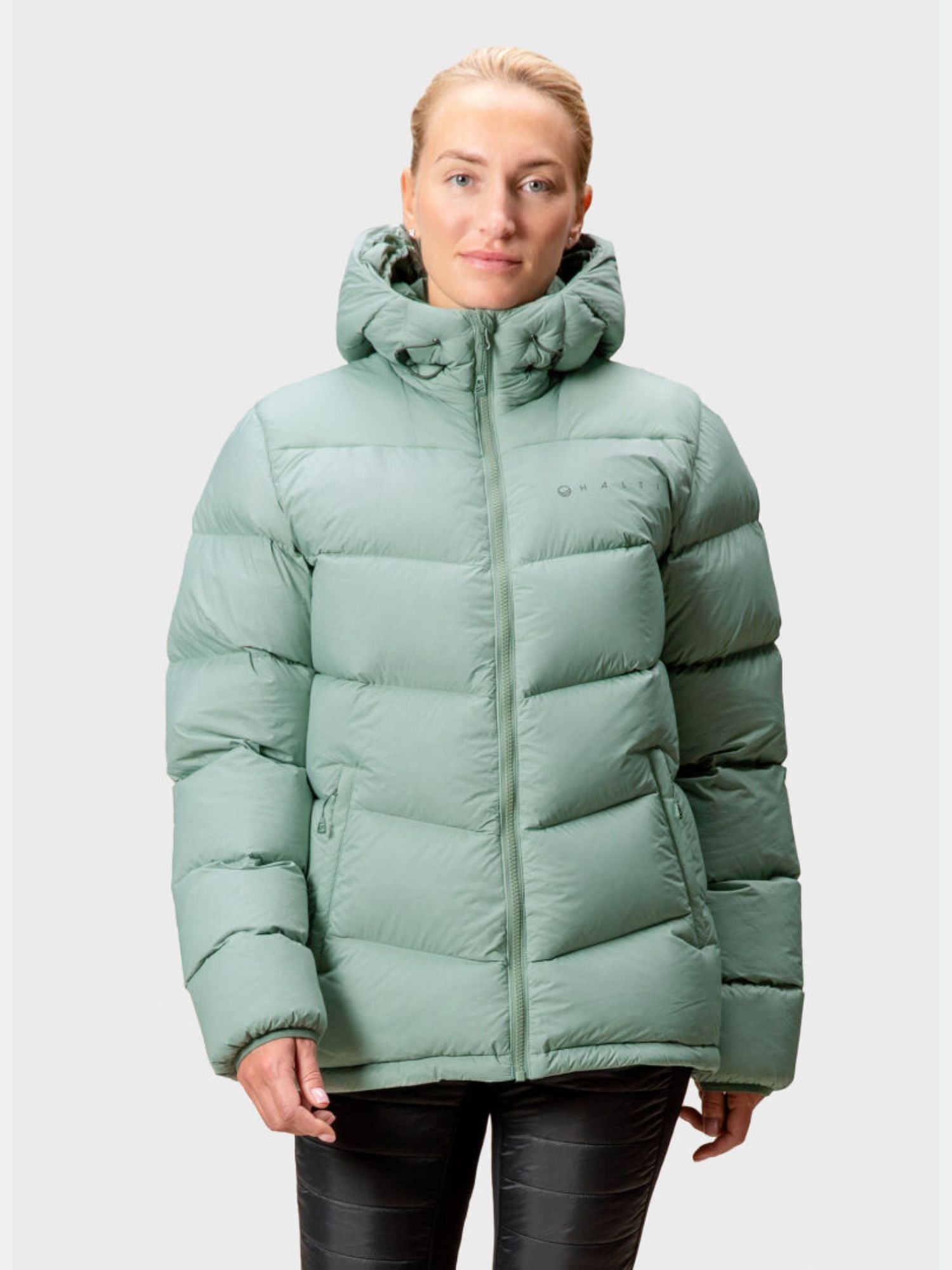 A woman wears the Halti Versant Down Jacket in light green, standing against a plain light gray background.