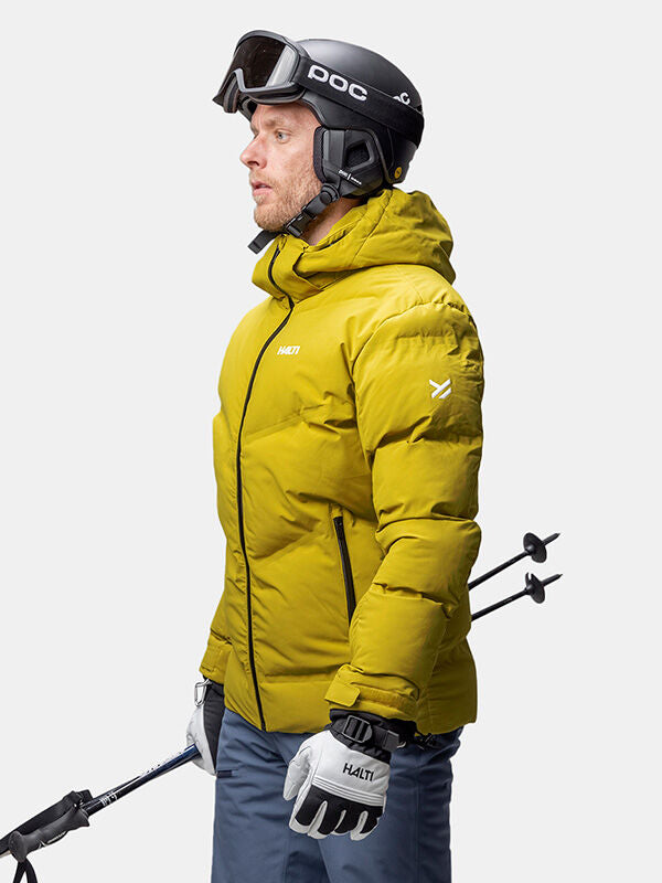 Person in a Halti Nordic Arcty II Ski Jacket with helmet, goggles, and ski poles stands against a plain background.