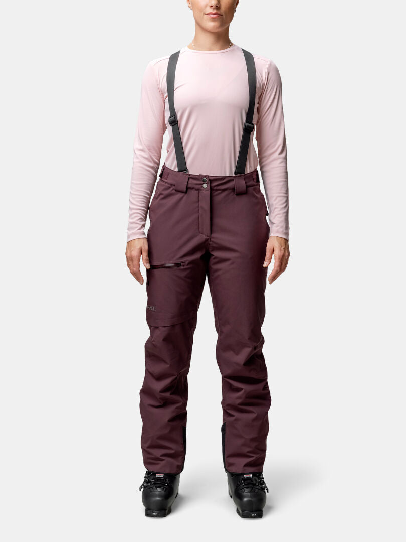 A person faces forward in a light pink shirt and Halti Carvey II DX Women's maroon ski pants with suspenders and black boots.
