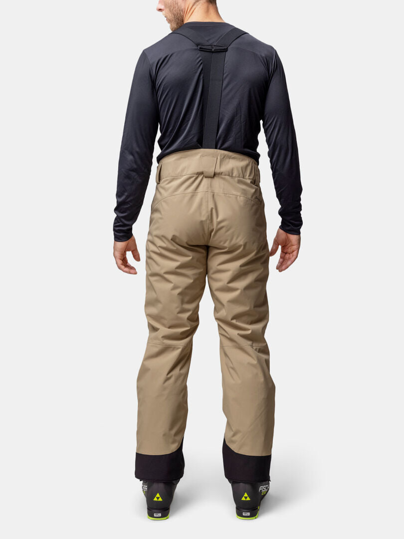 A person stands facing away in Halti Carvey II DX Ski Pants with suspenders, a black shirt, and ski boots.