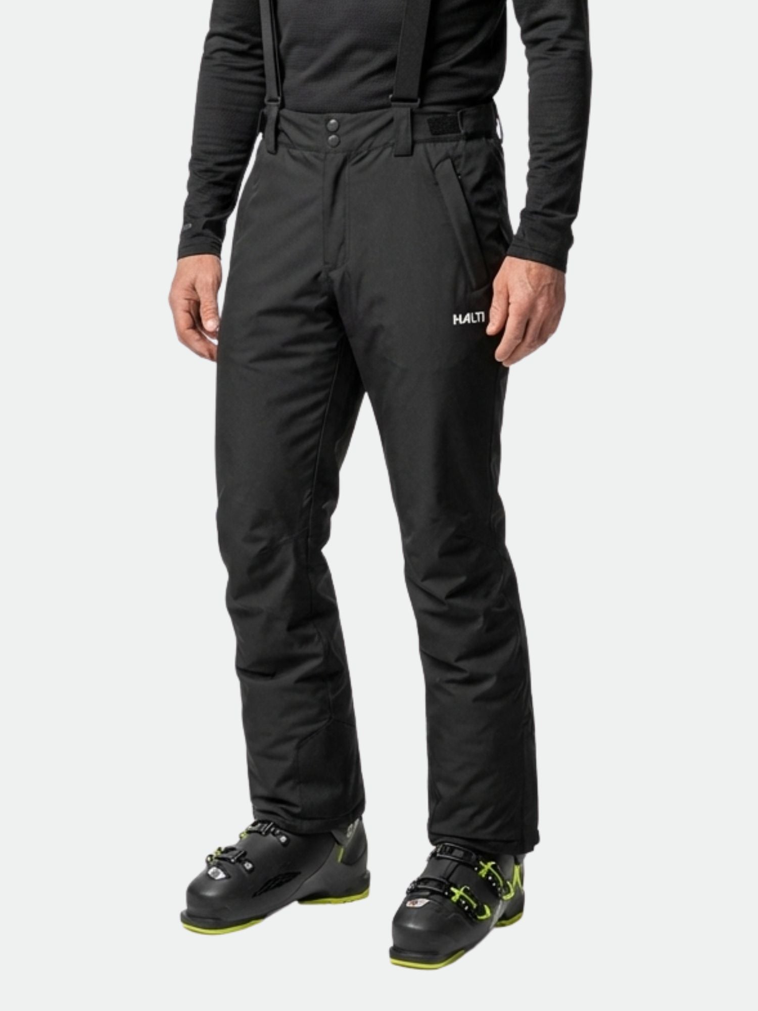 A man wearing Halti Glades II DX Ski Pants, a black long-sleeve shirt, and black ski boots.
