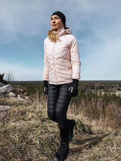 A woman wears Halti Veidnes Insulation Pants on a grassy hill with forest and clouds in the background.
