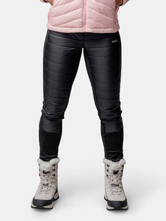 A person in a pink jacket, Halti Veidnes Insulation Pants Womens, and gray fur-trimmed boots stands against a white background.