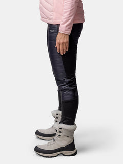 Woman in a light pink jacket, Halti Veidnes Insulation Pants Womens, and beige fur-trimmed boots stands sideways.