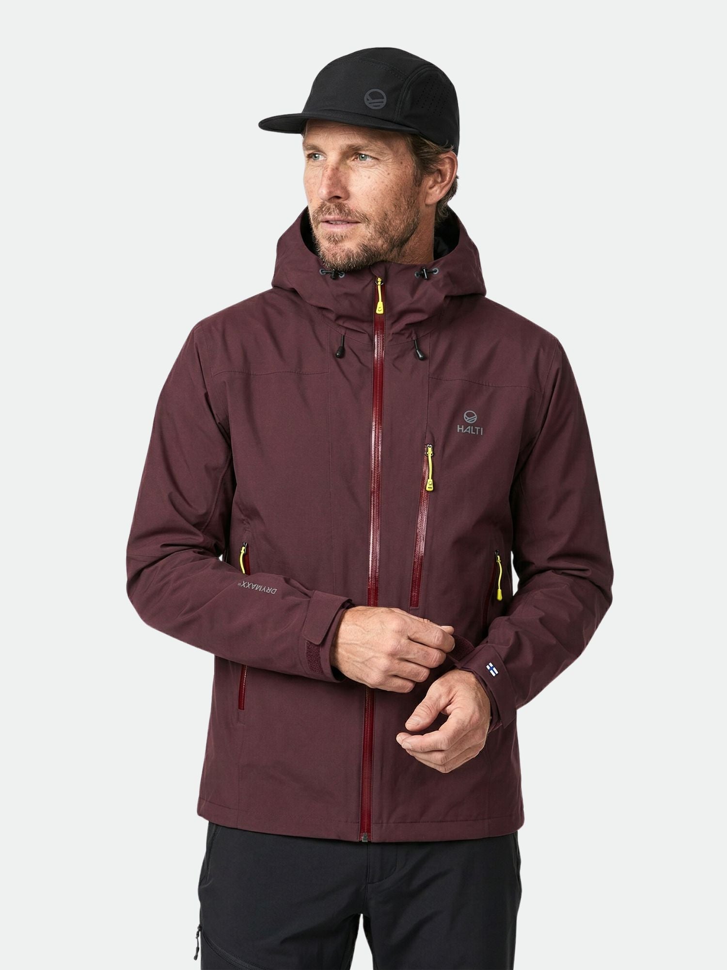 A man wears a maroon Halti Juonto DrymaxX Shell Jacket and black cap against a plain light background.