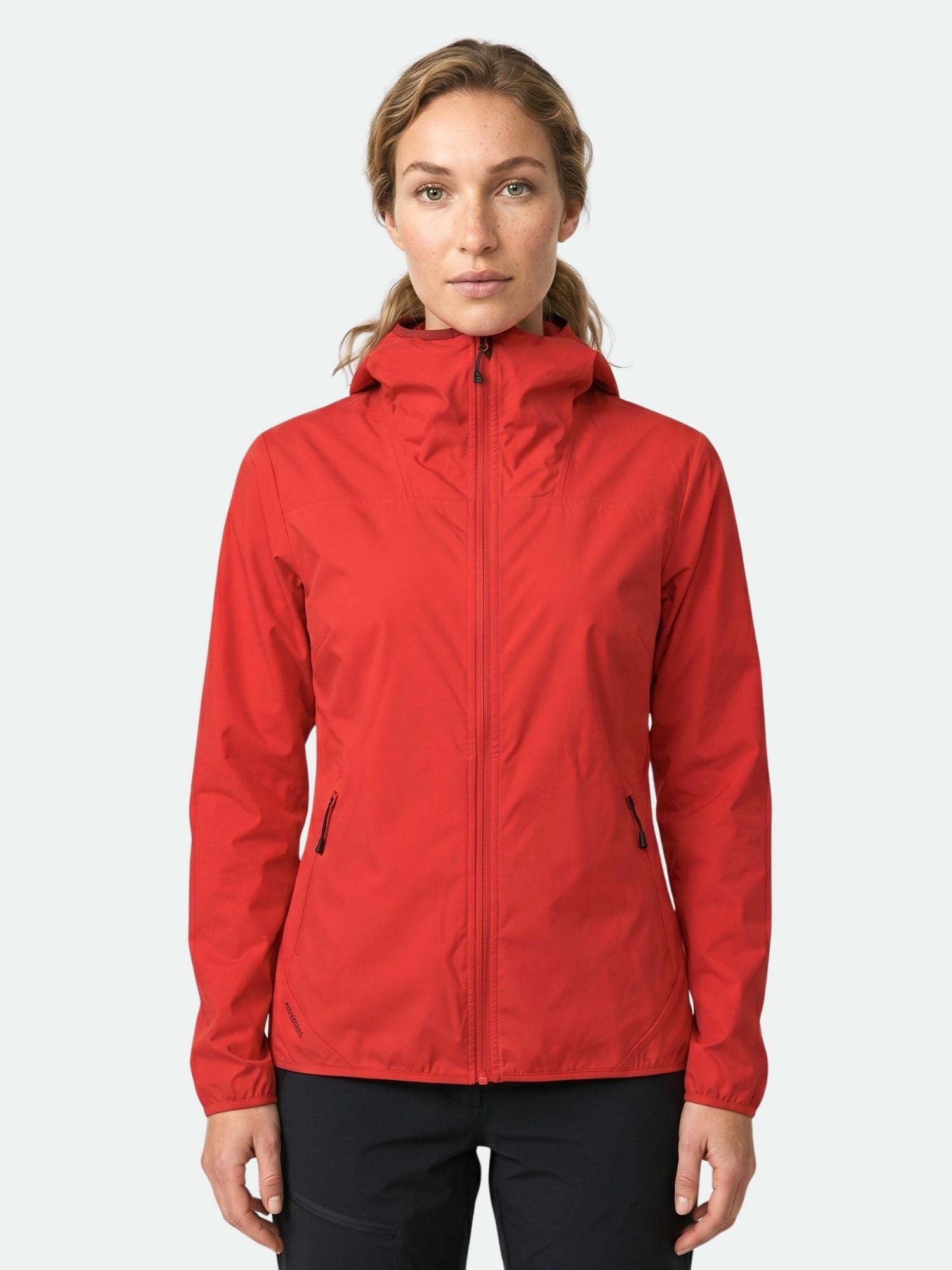 A woman in a red Halti Pallas Women's Lite X-stretch jacket and black pants stands facing forward on a light background.