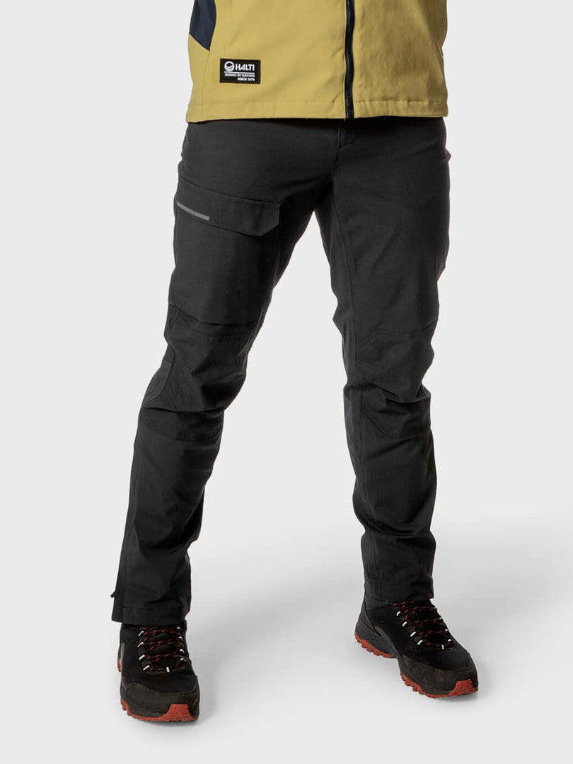 A person wears Halti Hiker Men's DrymaxX Pants, black shoes, and a yellow jacket on a plain background.