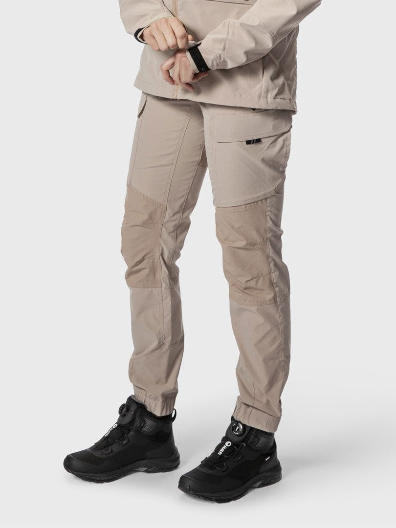 Woman stands against a plain background wearing Halti Hiker Womens Lite Outdoor Pants in beige and black shoes.