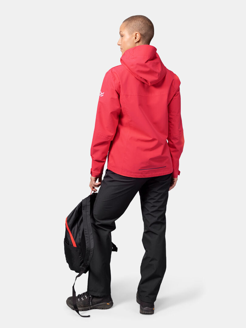 A person in a red Halti Forter DX Shell Jacket and black pants holds a black and red backpack in their left hand.