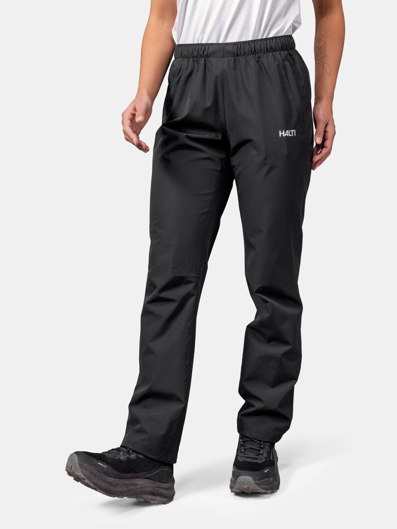 A person in Halti Forter DX Shell Pants, black hiking shoes, and a white shirt, ready for outdoor weather protection.