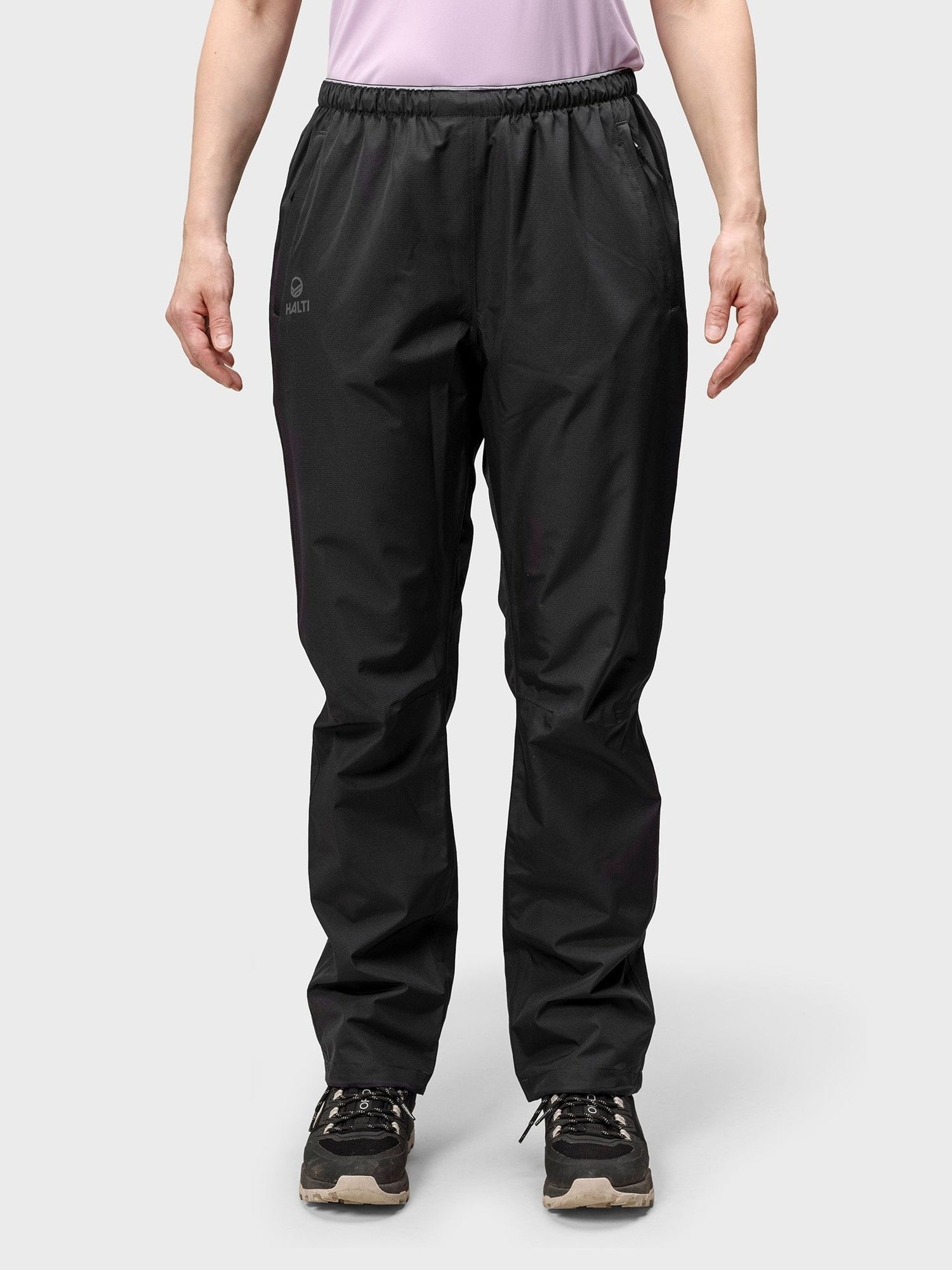 A person in Halti Forter DX Shell Pants and a light purple top stands against a plain background.