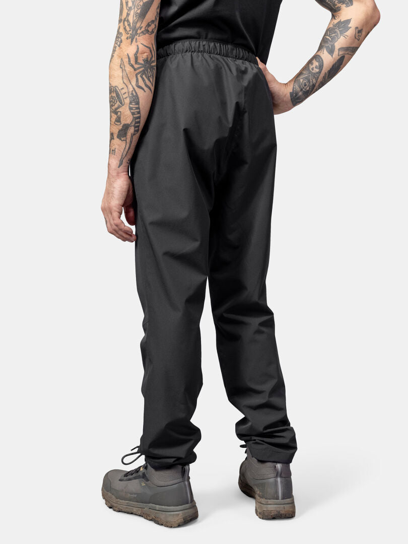 Person with tattoos wears Halti Forter DrymaxX Shell Pants, standing back to camera against a plain background.