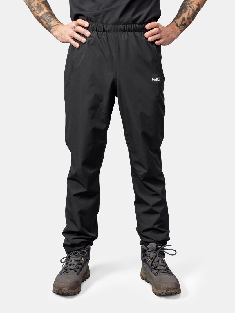 Person wearing Halti Forter DrymaxX Shell Pants and hiking boots, with a black shirt, against a plain light background.