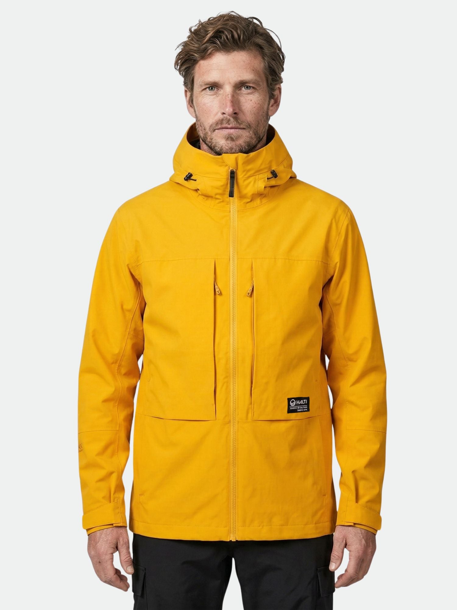 A man faces forward wearing the Halti Hiker II DrymaxX Shell Jacket Men's in bright yellow and black pants.